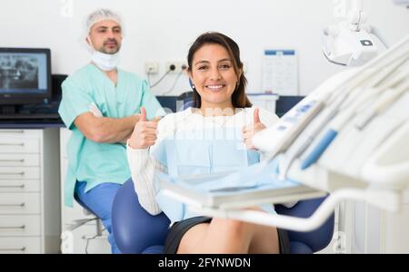 Ritratto di sorridente soddisfatta donna americana che visita dentista dando pollici in su Foto Stock