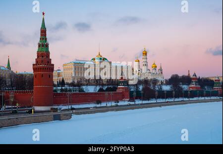 Vista pittoresca dell'insieme architettonico del Cremlino di Mosca sulla riva del fiume Moskva coperto di neve durante il tramonto in inverno, la Russia Foto Stock