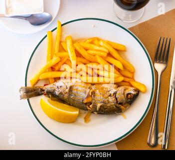 Pesce salpa fritto con patate e limone primo piano su un piatto Foto Stock