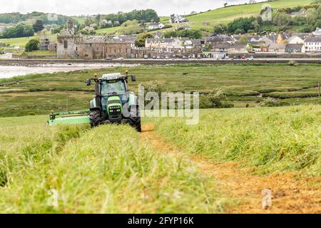 Timoleague, West Cork, Irlanda. 29 maggio 2021. In una giornata colma ma secca e umida con il Frate Francescano Timoleague che domina lo sfondo, Míchael McCarthy, azienda casearia con suo fratello Richard, taglia un campo di erba per insilato con un trattore Deutz-Fahr Agrotron K610 e un rasaerba John Deere 1360. Credit: AG News/Alamy Live News Foto Stock