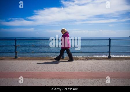 Donna anziana che cammina sul lungomare con orizzonte lontano Foto Stock