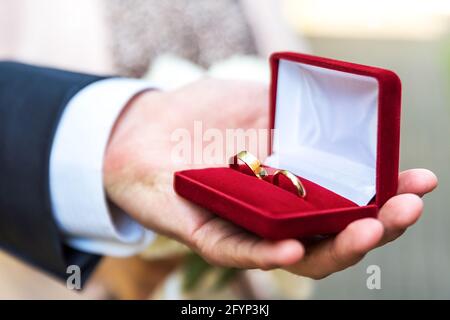 Anelli di nozze in una scatola tenuta in una mano maschio. Simbolo del matrimonio. Preparazione per il matrimonio. Foto Stock