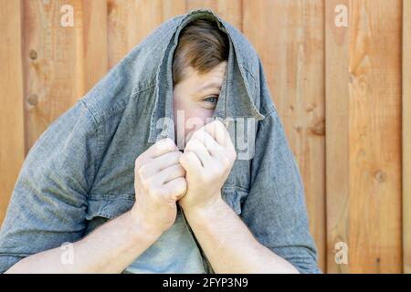 Uomo divertente, mettere una camicia sulla testa e porri con un occhio, sullo sfondo di un muro di legno. Foto Stock