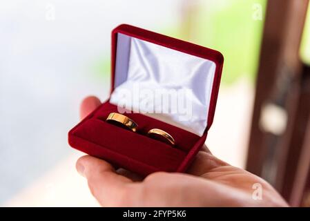 Anelli di nozze in una scatola tenuta in una mano maschio. Simbolo del matrimonio. Preparazione per il matrimonio. Foto Stock