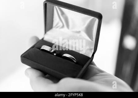 Anelli di nozze in una scatola tenuta in una mano maschio. Simbolo del matrimonio. Preparazione per il matrimonio. Foto Stock