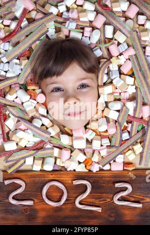 Felice carta anno nuovo. Volto di una ragazza caucasica felice seguito da un sacco di marshmallows colorati. Testo 2022 da gelatina Foto Stock