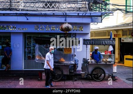 Un uomo anziano che indossa una maschera, passa davanti a un gruppo di bancarelle di cibo a Chinatown, Bangkok, Thailandia Foto Stock