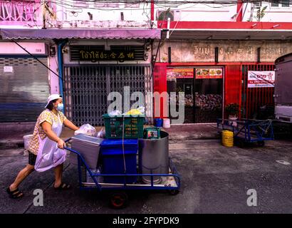 Un venditore di strada donna spinge il suo carrello alimentare lungo una strada stretta nella zona di Chinatown a Bangkok, Thailandia. Foto Stock