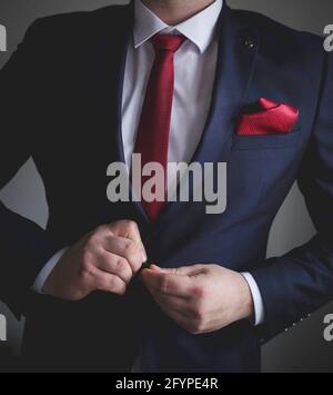 Uomo in una tuta blu e cravatta rossa che gli fa bottonare la giacca Foto Stock