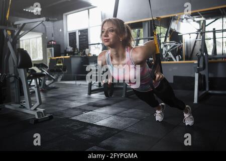 Donna atletica facendo esercizio di pressione sul petto su sistema trx trainer, spazio di copia Foto Stock