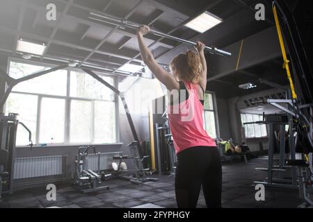 Vista posteriore di un'atleta irriconoscibile che solleva il barbell, facendo un esercizio di pressione Foto Stock