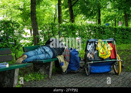 Un uomo senza casa dorme su una panchina del Theresienwiese a Monaco, dove l'Oktoberfest si svolge di solito ogni anno. Foto Stock