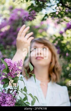 Ritratto autentico candido degli anni '40 della donna bionda caucasica con fiori di lilla. donna di 30 40 anni godendo la vita in fiori lilla sfondo natura Foto Stock