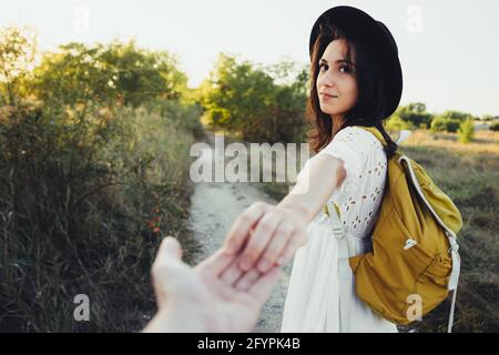 Seguimi. Giovane donna in cappello che tiene la mano e che conduce l'uomo al bellissimo paesaggio di tramonto natura. Vista dal lato posteriore, POV. Viaggio romantico in coppia, Foto Stock