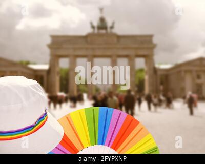 Donna LGBT caucasica matura a Berlino con ventola arcobaleno e nastro su cappello estivo bianco. Rainbow, simbolo dell'orgoglio gay LGBTQIA, la diversità. Donna che indossa Foto Stock