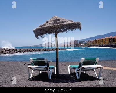 Vista dalla spiaggia di lava sull'Oceano Atlantico e la località 'Punta largaa' sulla costa meridionale dell'isola di Tenerife. In primo piano due vuoti Foto Stock