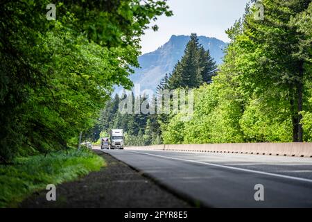 Due grandi trattori industriali semirimorchi per il trasporto di carichi commerciali in diversi semirimorchi che girano nella stessa direzione in autostrada strada con gre Foto Stock