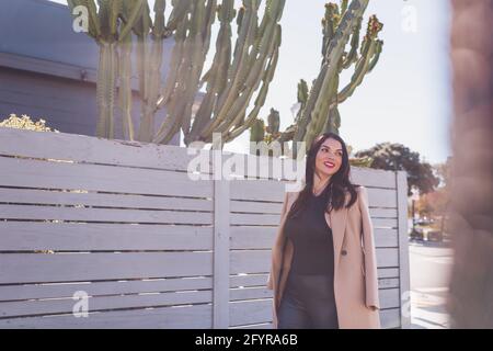 Donna d'affari sorridente che cammina per strada indossando un cappotto abbronzato. Foto Stock