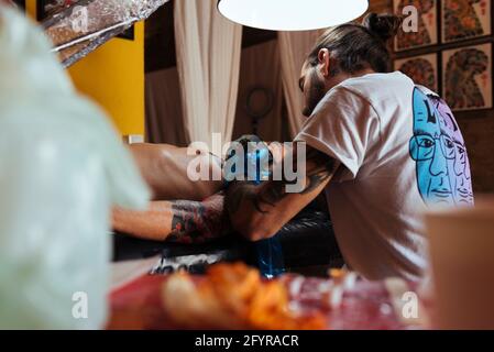 Vista posteriore dell'artista del tatuaggio che lavora sul braccio di un cliente nel suo studio. Foto Stock