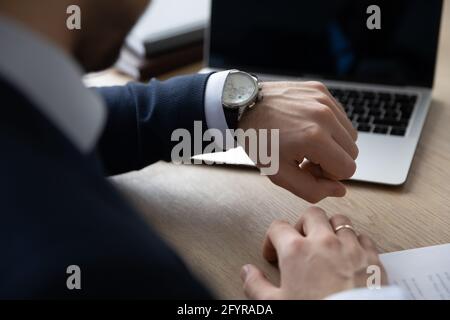 Uomo d'affari puntuale che controlla il tempo sul posto di lavoro, consultando orologio da polso di lusso Foto Stock