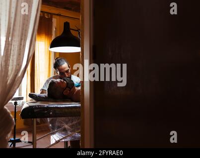 Vista attraverso le tende di un artista tatuaggio che lavora con un cliente. Foto Stock