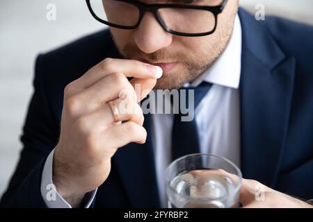 Serio giovane uomo d'affari che tiene un bicchiere d'acqua, prendendo pillole Foto Stock