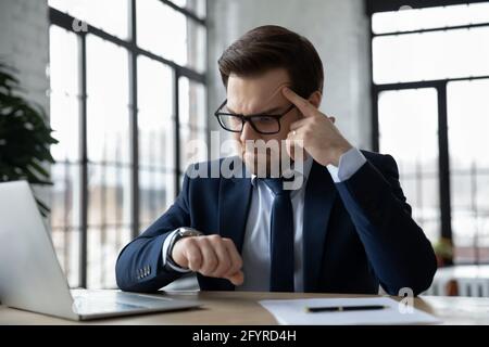 Uomo d'affari interessato seduto sul posto di lavoro e consulente orologio da polso Foto Stock