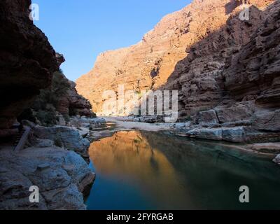 Il paesaggio roccioso, desolato, con piscina d'acqua nella gola di Wadi Shab in piena luce del sole. In Oman. Foto Stock