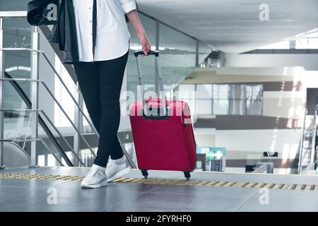 la donna che viaggia con i bagagli sale le scale dell'aeroporto o della stazione ferroviaria; le gambe e la valigia da vicino Foto Stock