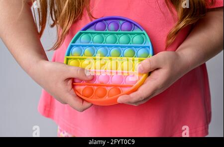 Ragazza capretto mano tenere nuovo giocattolo sensoriale - pop it. Colore arcobaleno, bolle concave e convesse. Forma di silicone Foto Stock