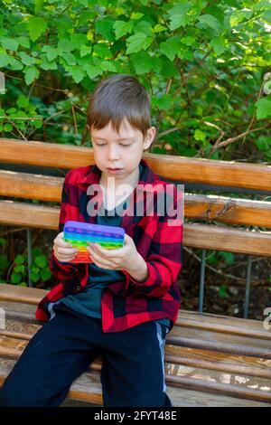 bambino di 8 anni che gioca con popit nel parco. bambino felice con giocattolo. bambino che indossa abiti casual estivi luminosi. pop-up multicolore. Antistress p Foto Stock