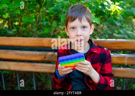 bambino di 8 anni che gioca con popit nel parco. bambino felice con giocattolo. bambino che indossa abiti casual estivi luminosi. pop-up multicolore. Foto Stock