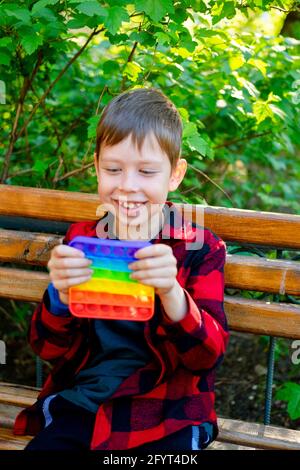 bambino di 8 anni che gioca con popit nel parco. bambino felice con giocattolo. bambino che indossa abiti casual estivi luminosi. pop-up multicolore. Foto Stock