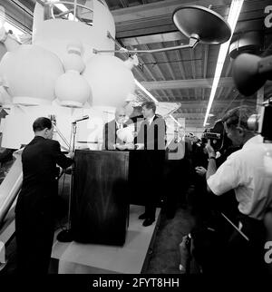 12 settembre 1962 il presidente John F. Kennedy (al leggio) fa commenti, dopo un tour delle mostre di veicoli spaziali all'interno di un hangar presso il Rich Building del presidiato Spacecraft Center, Houston, Texas. Il presidente Kennedy possiede un modello in scala del modulo di comando Apollo, presentato a lui dal direttore del presidiato Spacecraft Center, il dottor Robert Gilruth; un mock-up del lander lunare (noto anche come 'il Bug') si trova sullo sfondo. In piedi: Amministratore della National Aeronautics and Space Administration (NASA), Dr. James E. Webb; Governatore del Texas, Price Daniel; Foto Stock