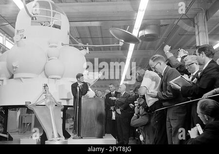 12 settembre 1962 il presidente John F. Kennedy (al leggio) trasmette le sue osservazioni, dopo un tour delle mostre di veicoli spaziali all'interno di un hangar presso il Rich Building del presidiato Spacecraft Center, Houston, Texas. Il presidente Kennedy possiede un modello in scala del modulo di comando Apollo, presentato a lui dal direttore del presidiato Spacecraft Center, il dottor Robert Gilruth; un mock-up del lander lunare (noto anche come 'il Bug') si trova a sinistra in background. In piedi: Direttore delle operazioni per il progetto Mercury, Dr. Walter C. Williams; amministratore associato della National Aeronautics and Space Administration Foto Stock