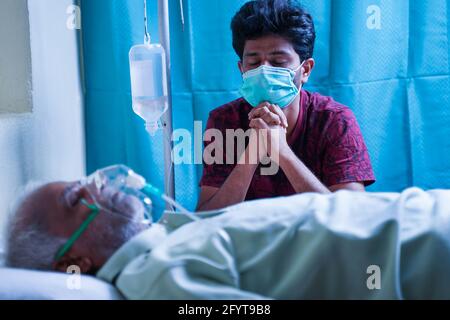 Preoccupato ha sottolineato il giovane uomo che pregava per suo padre di recuperare dall'infezione covid 19 mentre respirava su maschera di ossigeno ventilatore in ospedale - Foto Stock