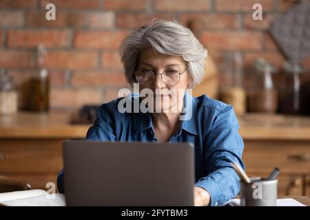 Donna seria che lavora su un computer portatile seduto al tavolo in cucina Foto Stock