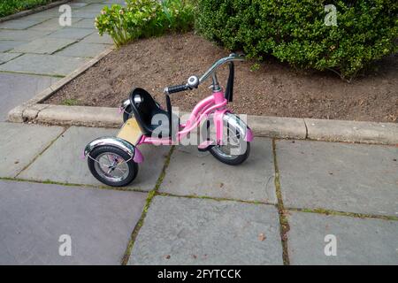 Triciclo a tre ruote per ragazze sul marciapiede in ardesia del parco Foto Stock