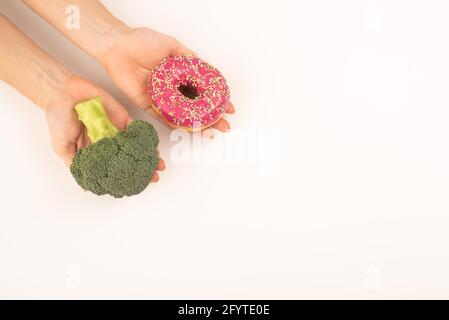 Confronto delle abitudini alimentari. Donna che tiene broccoli e ciambella su sfondo bianco. Spazio di copia Foto Stock