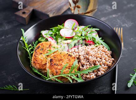 Cena sana. Ciotola per il pranzo con porridge di grano saraceno, cotolette di pollo fritte e insalata di arugula, cetriolo e rafano di verdure fresche. Foto Stock