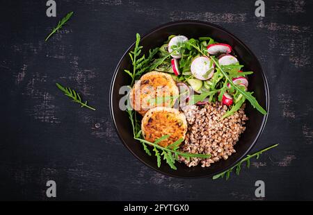 Cena sana. Ciotola per il pranzo con porridge di grano saraceno, cotolette di pollo fritte e insalata di arugula, cetriolo e rafano di verdure fresche. Vista dall'alto, appartamento la Foto Stock