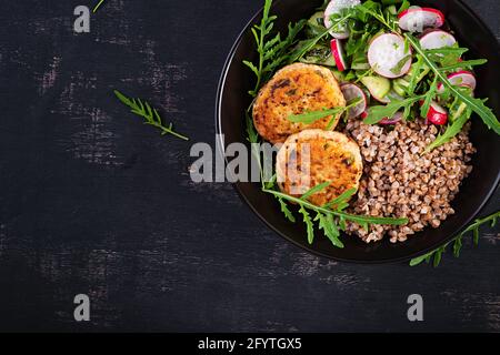 Cena sana. Ciotola per il pranzo con porridge di grano saraceno, cotolette di pollo fritte e insalata di arugula, cetriolo e rafano di verdure fresche. Vista dall'alto, appartamento la Foto Stock