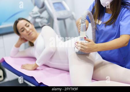 Donna in speciale tuta bianca con massaggio anticellulite con impianto termale Foto Stock