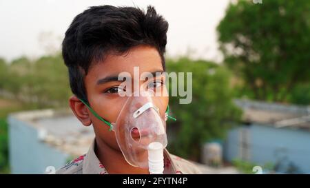 Un ragazzino che respira con la maschera di ossigeno a casa. Paziente infantile indiano infettato con la malattia di Covid 19. Ragazzo indiano che prende il trattamento di Asma, polmoni. Foto Stock