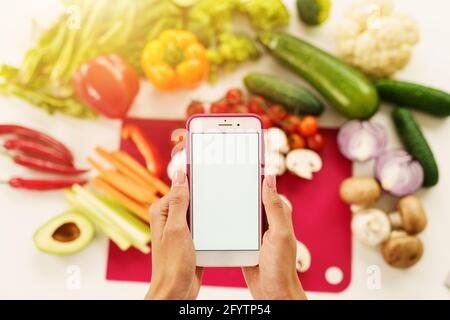 Cook segue una ricetta di verdure dallo smartphone Foto Stock