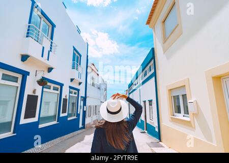Vista posteriore di una giovane donna turistica con cappello bianco camminando sulle strette strade del Portogallo meridionale in una giornata estiva soleggiata. Vacanze estive Foto Stock