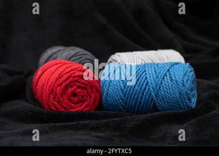 Corde e corde di cotone rosso, bianco, blu, grigio adatte per l'uso in lavori di ago e artigianato macramé su un panno nero Foto Stock