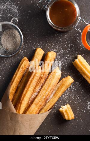 Churros con zucchero, cannella e caramello su sfondo scuro. Vista dall'alto Foto Stock