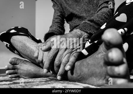 Un primo piano di piedi e mani di una donna anziana in India in bianco e nero. Foto Stock