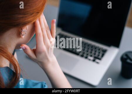 Primo piano vista posteriore di stanco frustrato giovane medico femminile in uniforme medica blu massaggiando templi, che soffrono di mal di testa Foto Stock